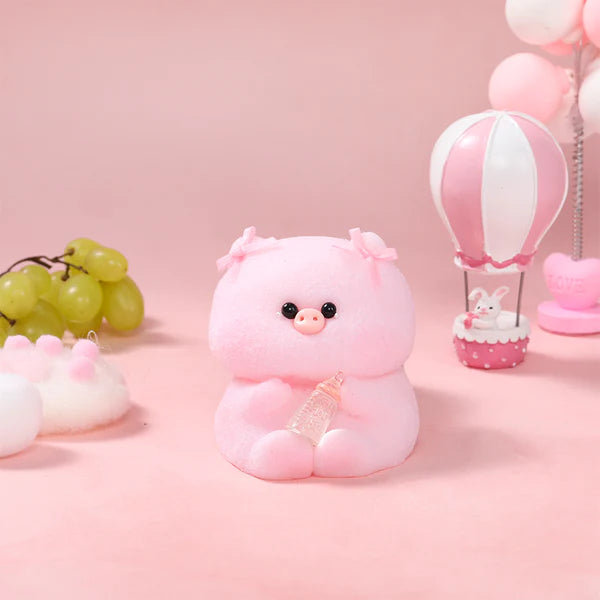 Pink piglet plush toy holding a small pink bottle, photographed on a pink tabletop with pastel decorations.